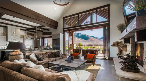 A spacious, modern living room with a cozy sofa, large windows, and a view of mountains outside.